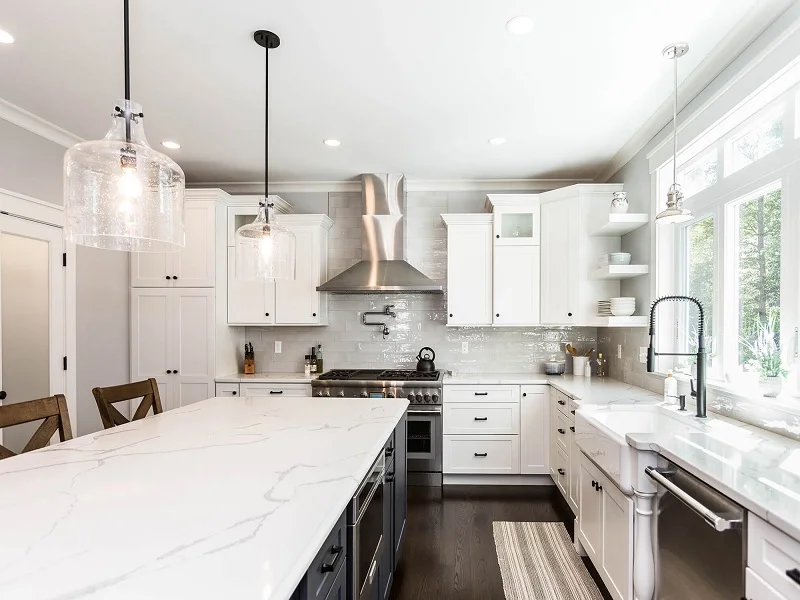 White kitchen with a long island, glass pendants and stainless steel range hood